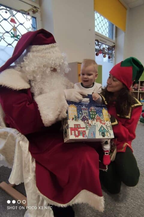 Mikołaj z elfem wręczają prezent dziecku