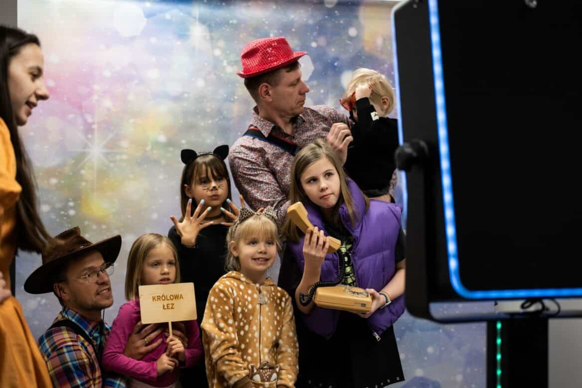 Dzieci w przebraniach pozują do zdjęcia przed fotobudką na balu karnawałowym.